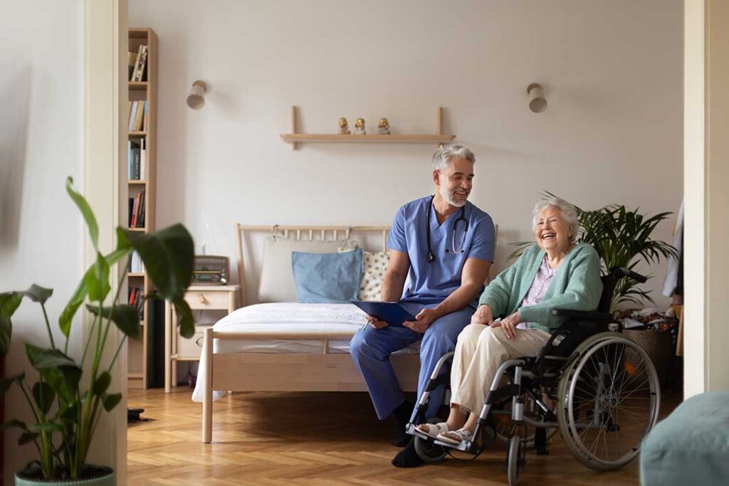 Older adult speaking with a caregiver in a bright assisted living apartment with a walker nearby.